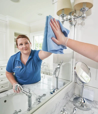 A uniformed Maid Brigade professional polishing a bathroom mirror